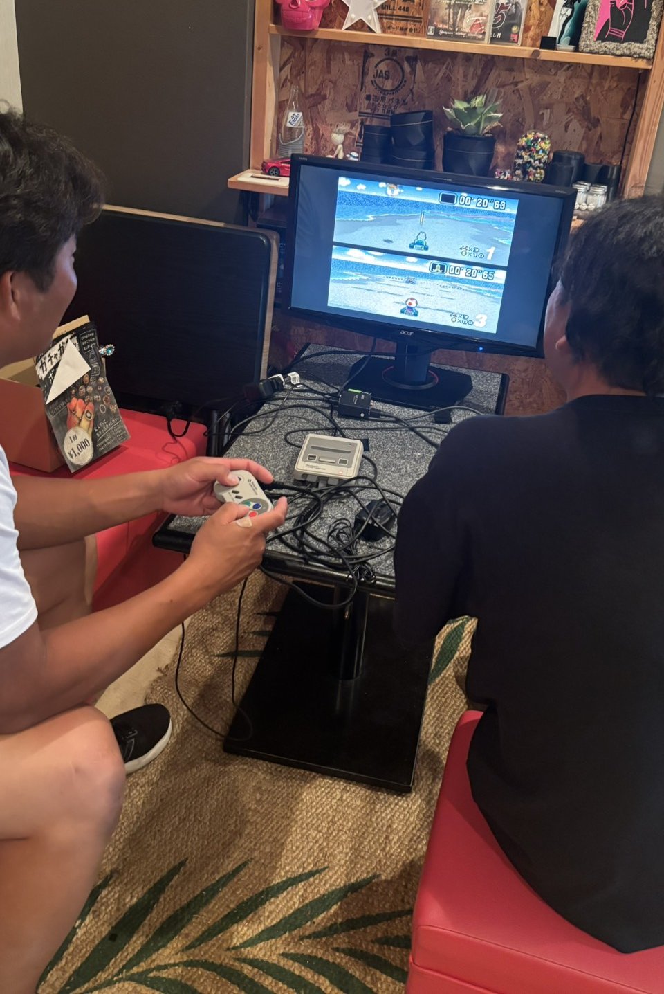 モニターの前に並んで座り、スーパーマリオカートで対戦する2人